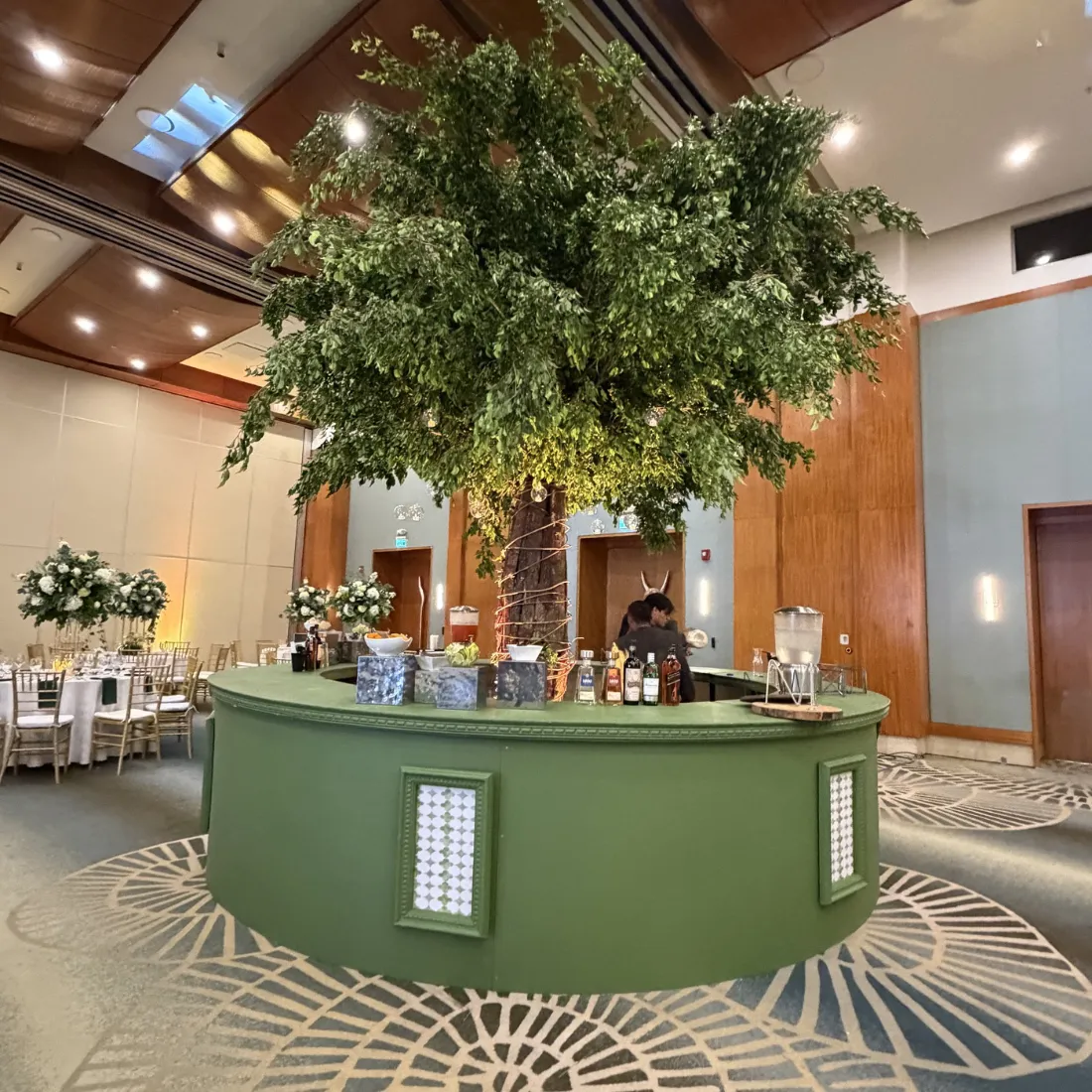 Barra verde circular bajo un árbol de follaje en salón de eventos